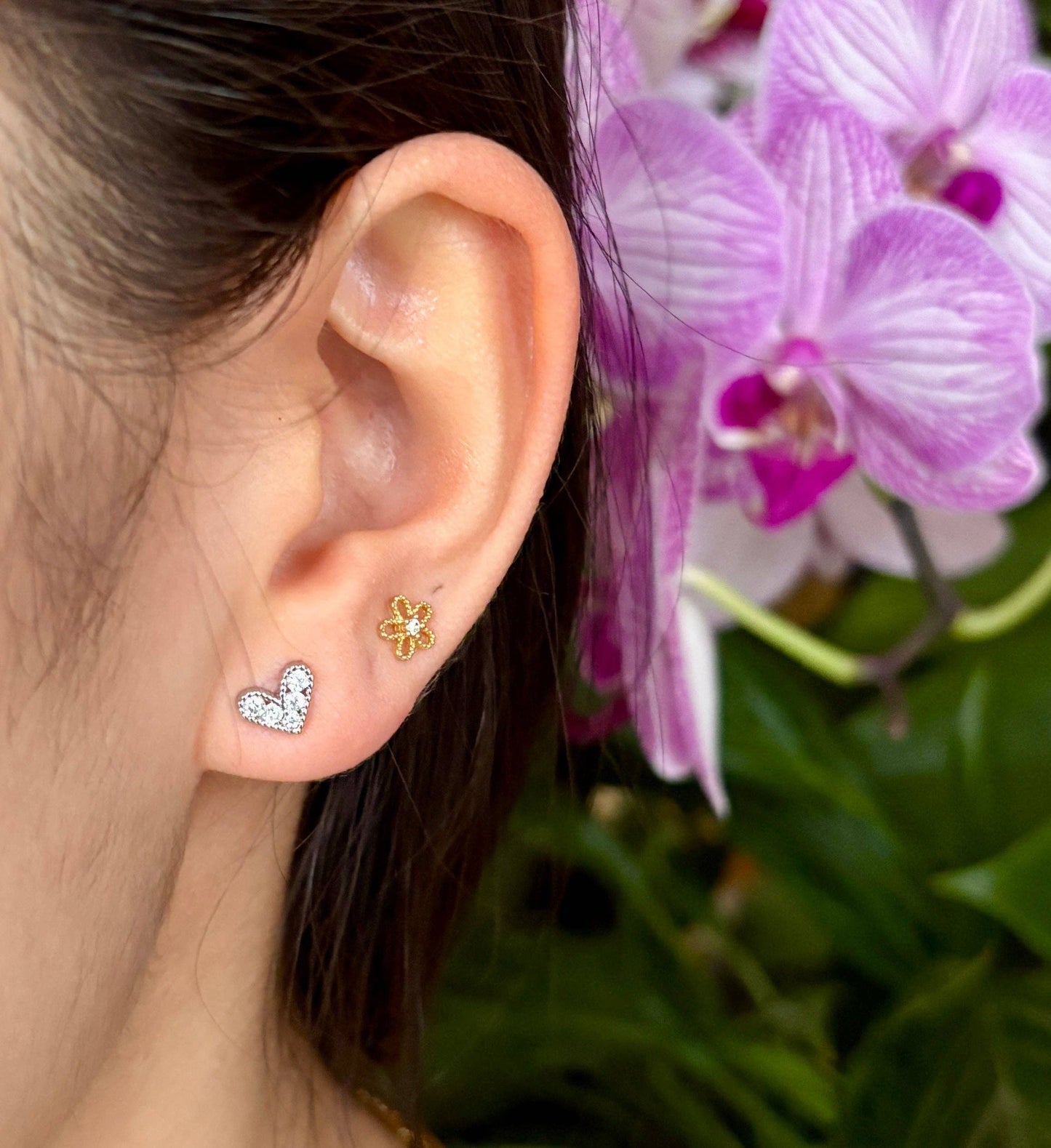 Close-up of an ear wearing two earrings with a blurred background of pink flowers.