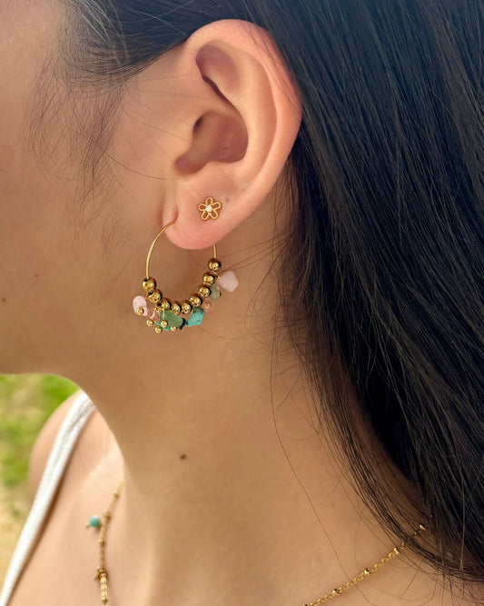 Close-up of a person wearing a gold hoop earring with colorful beads.