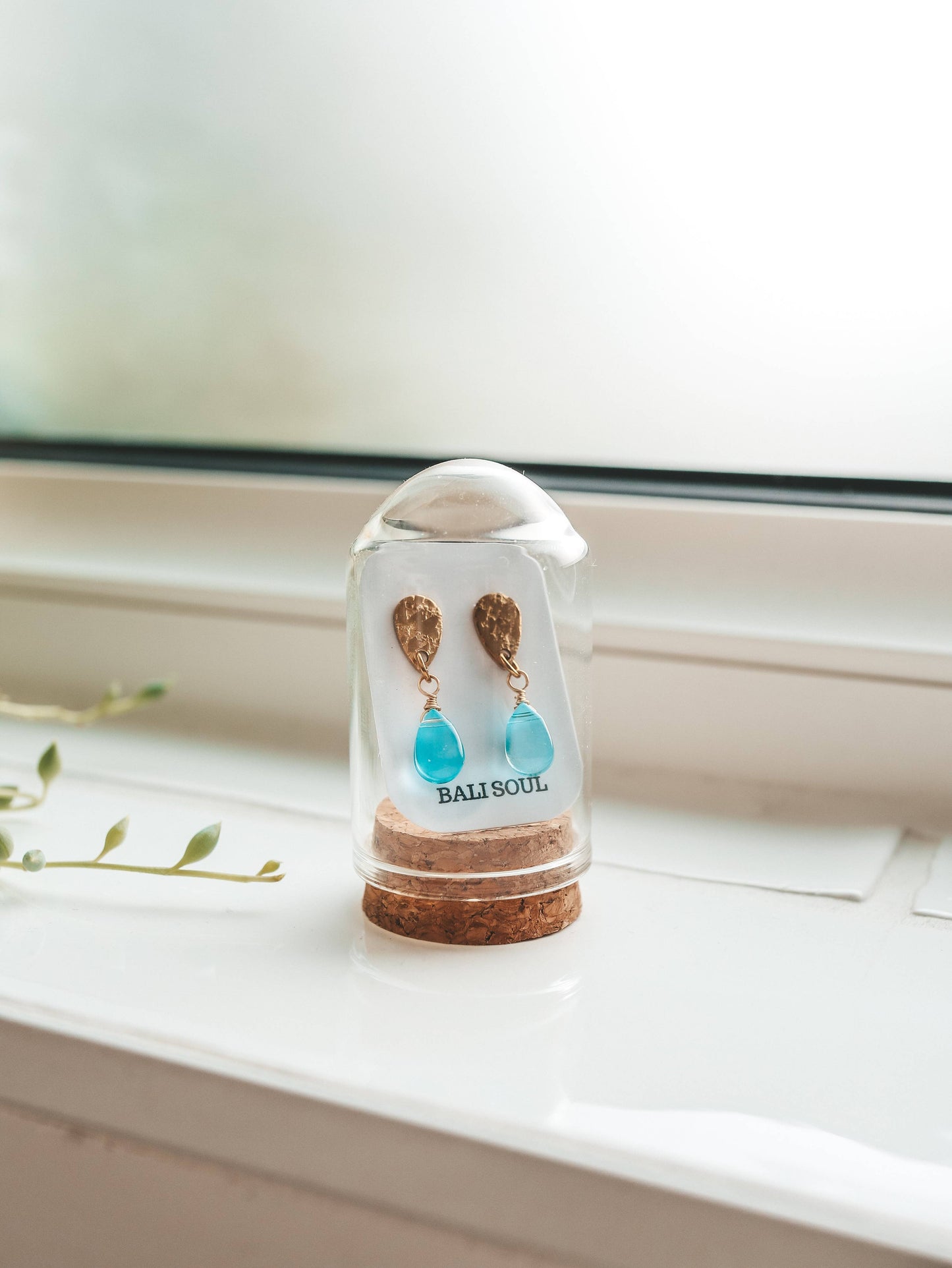 Turquoise earrings in a glass display case on a white surface with a blurred background