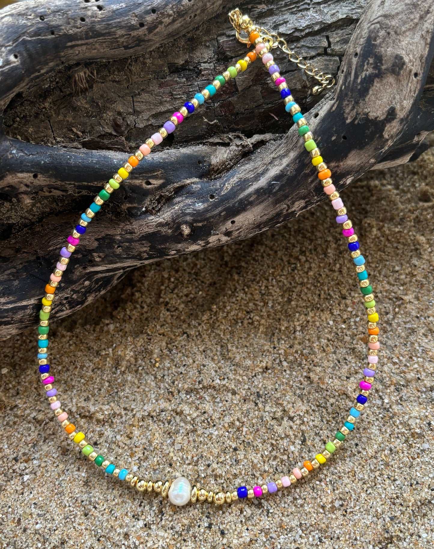 Colorful beaded necklace on a sandy surface with driftwood in the background