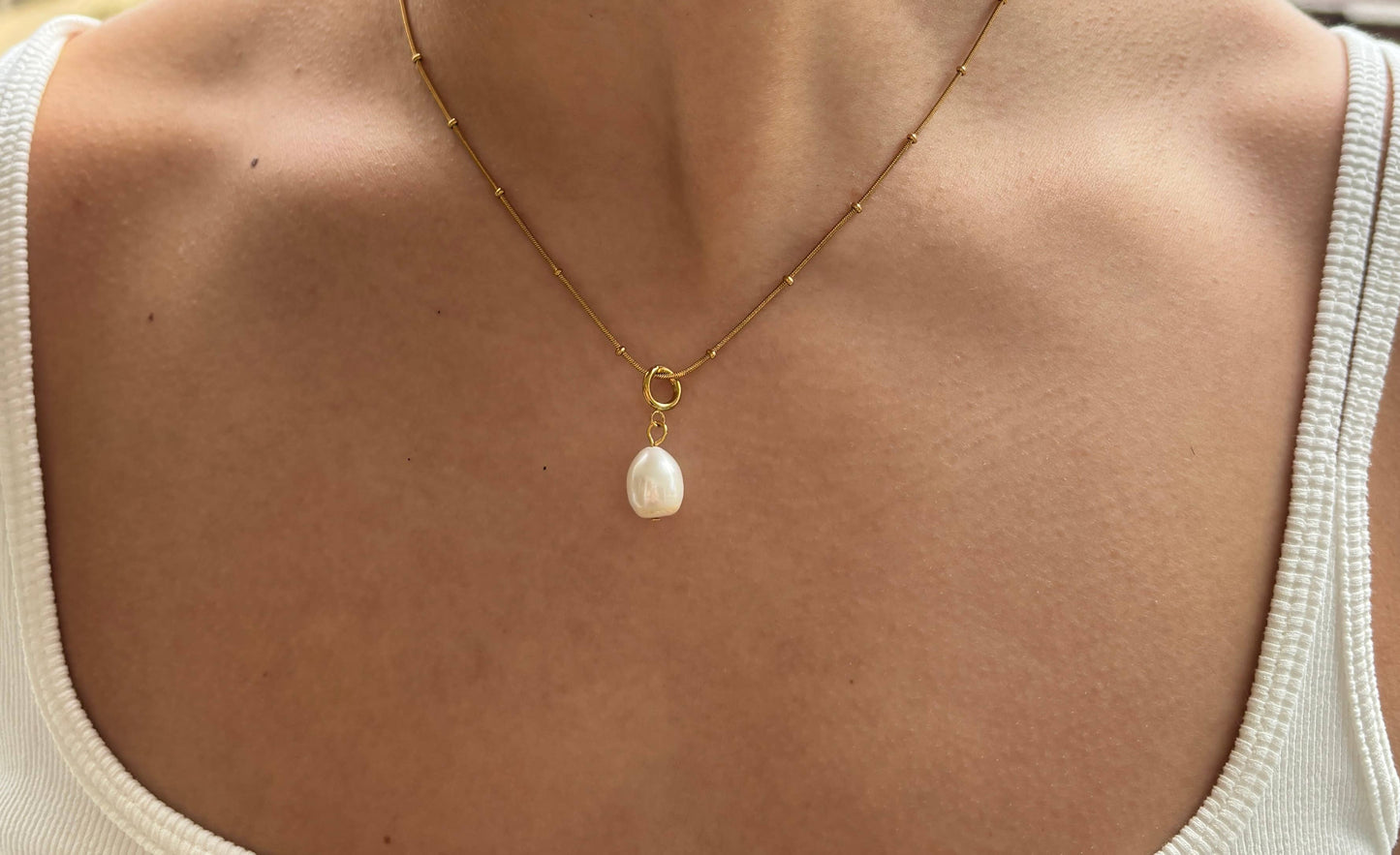 Gold necklace with a pearl pendant on a person wearing a white tank top.