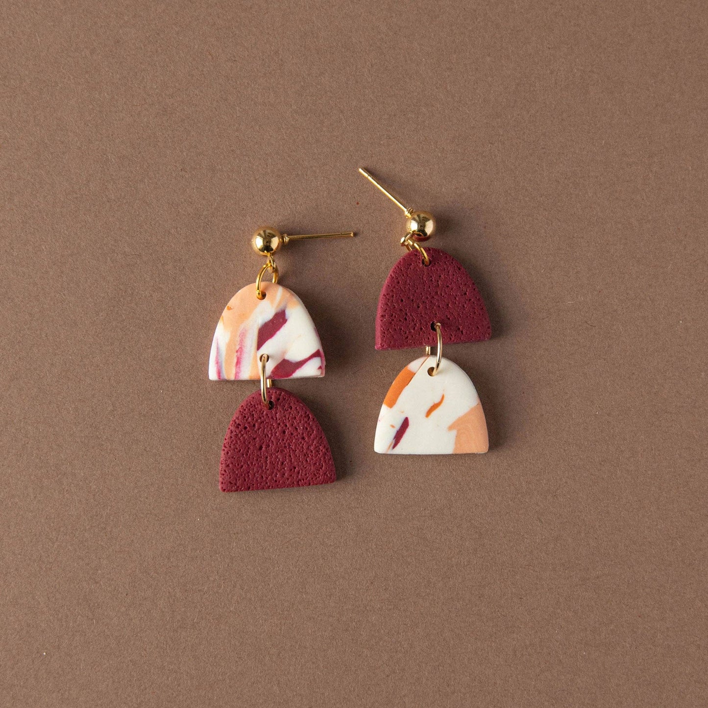 Handmade polymer clay earrings in berry pumpkin and peach tones with gold plated posts on background.