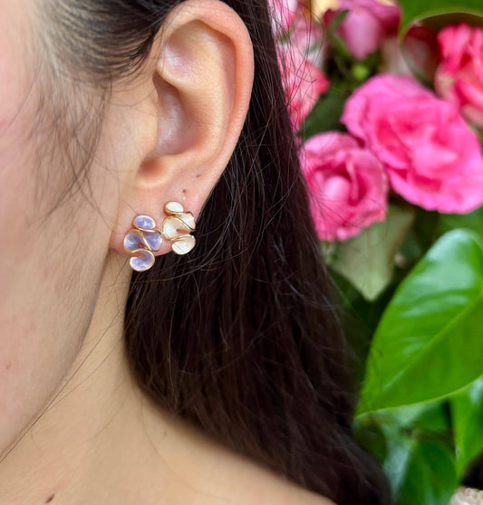 Close-up of an ear wearing a floral earring with pink flowers in the background