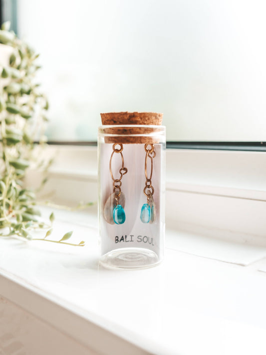 Jewelry set in a clear glass jar with cork lid on a white surface.