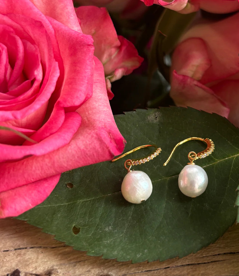 Pearl earrings on a green leaf with pink roses in the background
