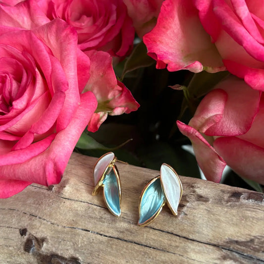Pair of earrings with gold and blue accents on a wooden surface with pink roses in the background