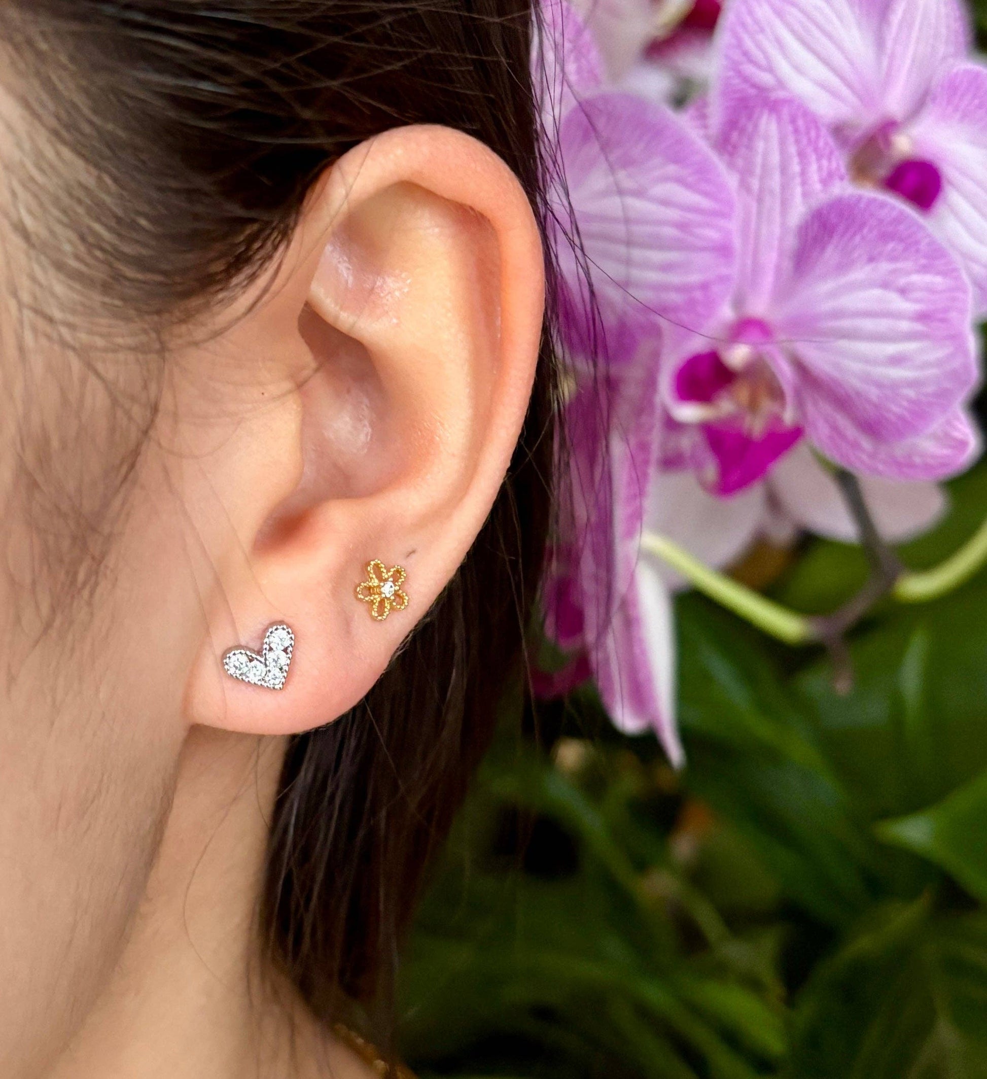 Close-up of an ear wearing two earrings with a blurred background of pink flowers.