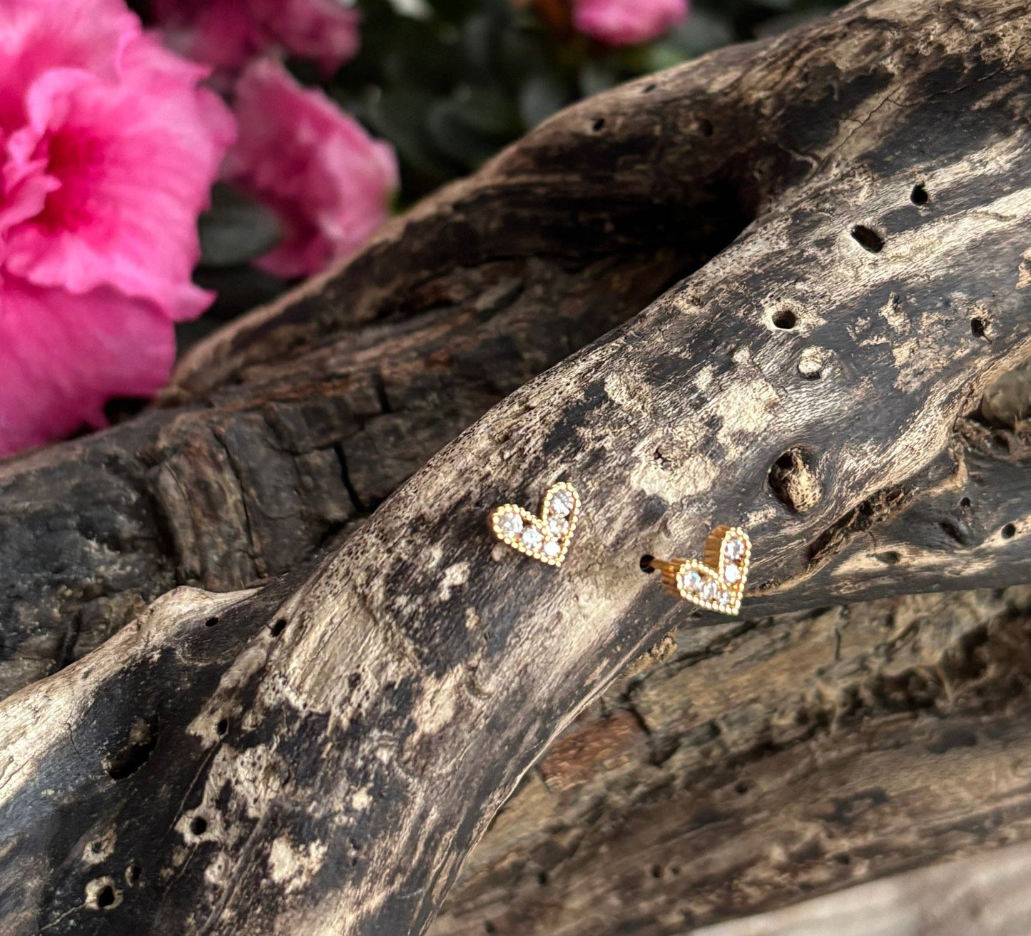 Heart-shaped earrings on a piece of driftwood with pink flowers in the background