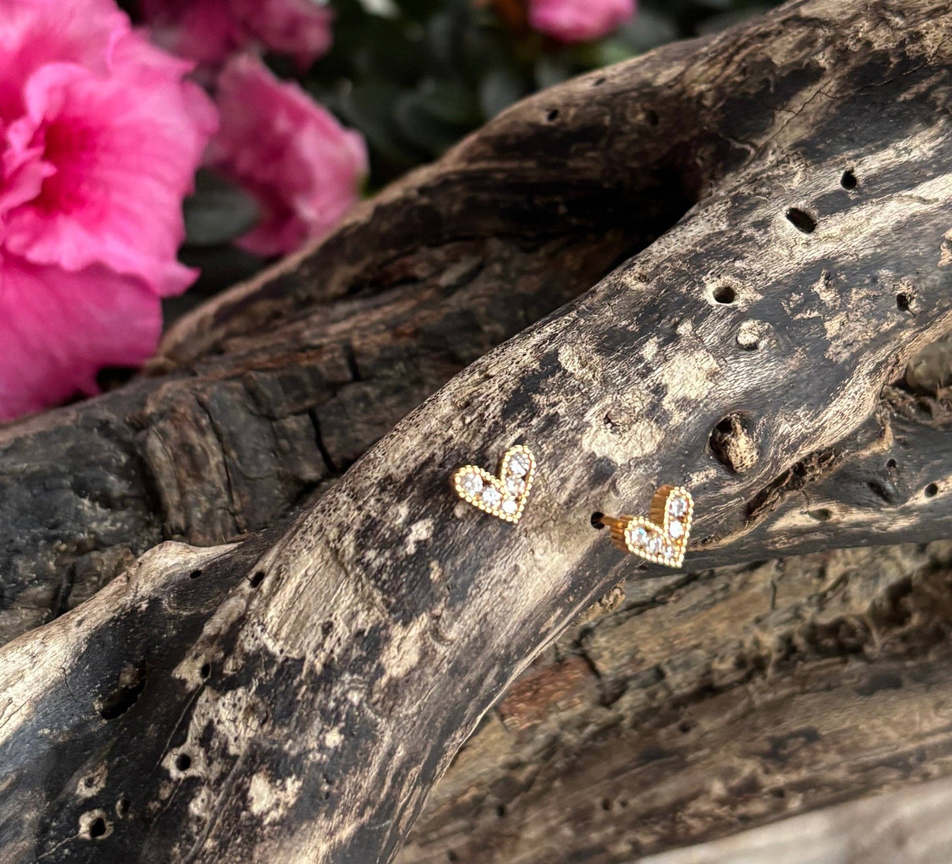 Heart-shaped earrings on a piece of driftwood with pink flowers in the background