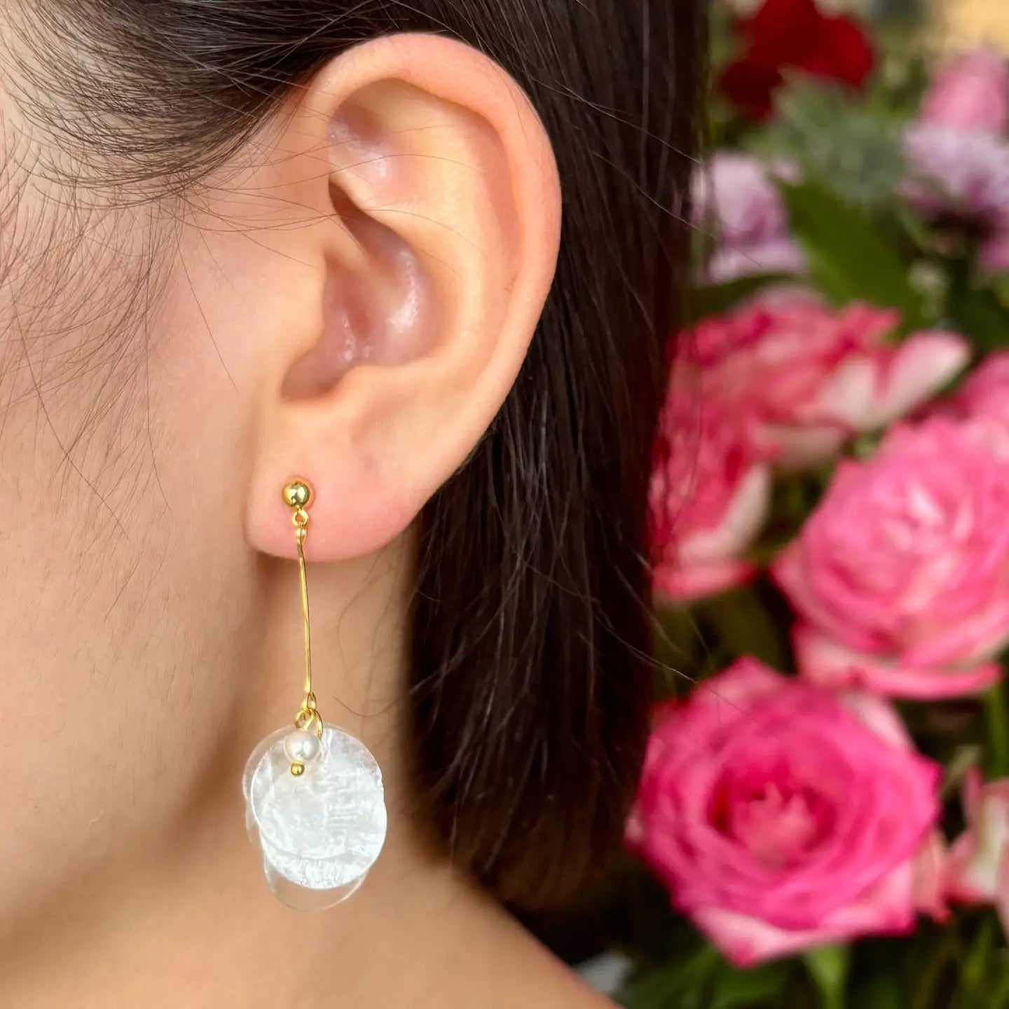 Close-up of an ear wearing gold earrings with a blurred background of pink flowers