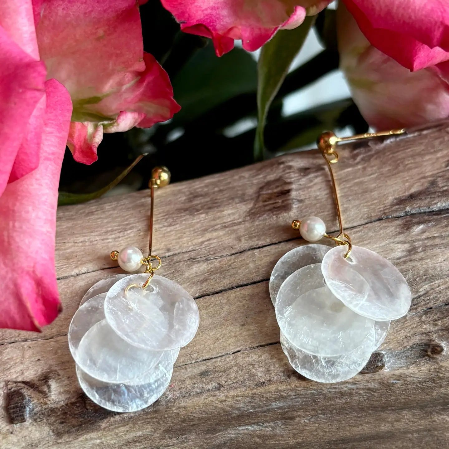 Clear circular earrings with gold accents on a wooden surface with pink flowers in the background