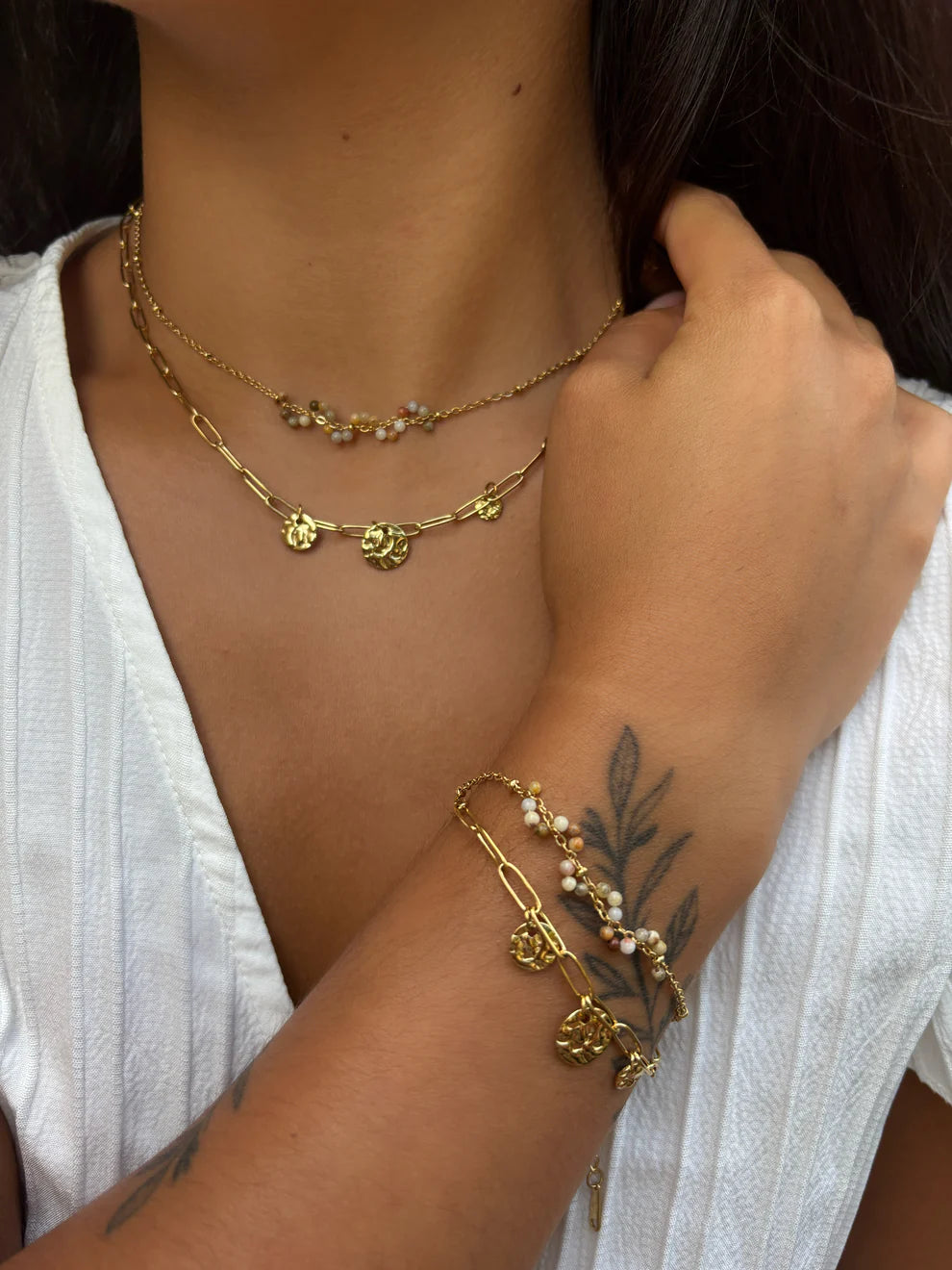 Close-up of a person wearing gold necklaces and bracelets with a white top.