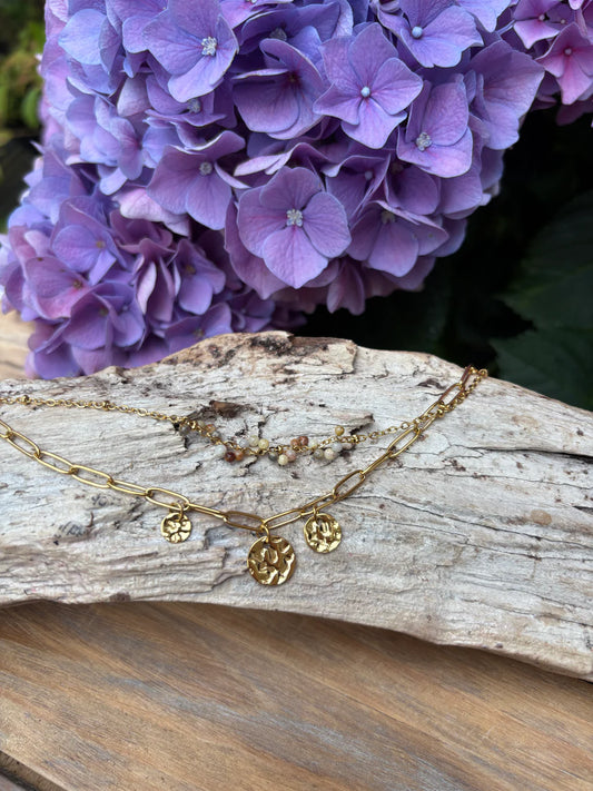 Gold necklace with floral pendants on a wooden surface with purple flowers in the background
