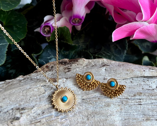 Gold necklace and earrings with turquoise stones on a wooden surface with pink flowers in the background