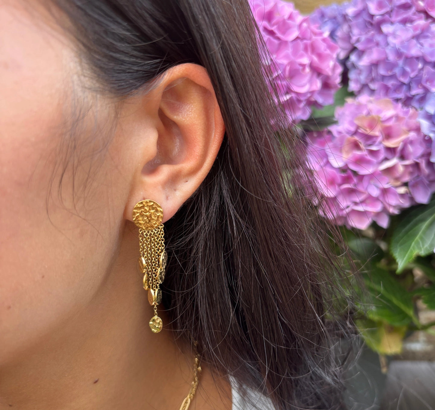 Gold earring worn by a person with purple flowers in the background