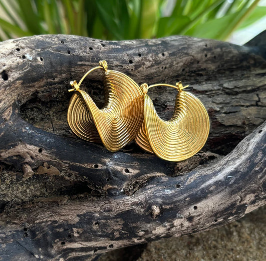 Gold hoop earrings on a piece of driftwood with a natural background