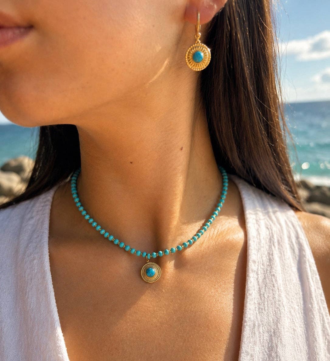 Woman wearing a turquoise necklace and earrings with a beach background