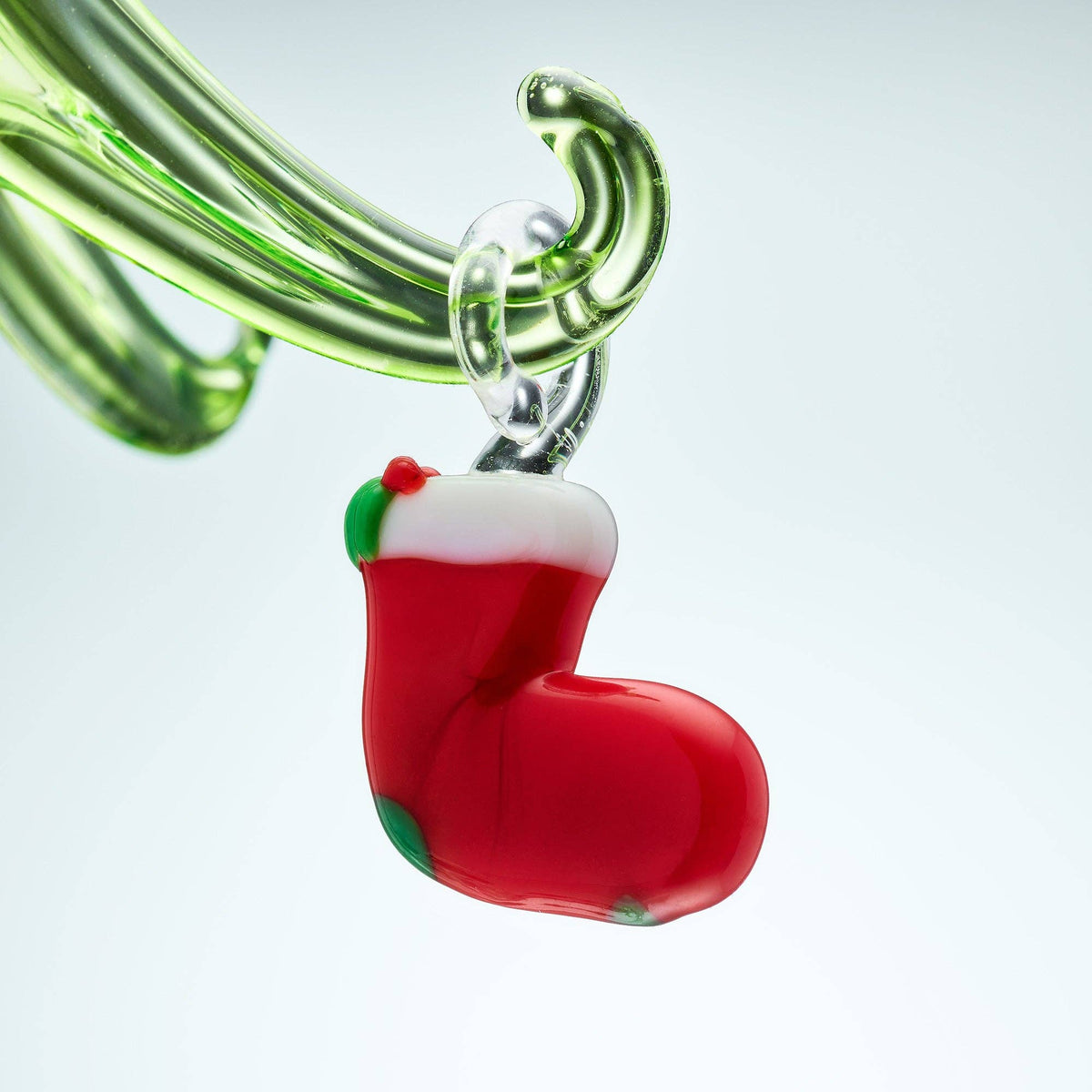 Glass smoking accessory shaped like a red stocking with green accents on a light gray background