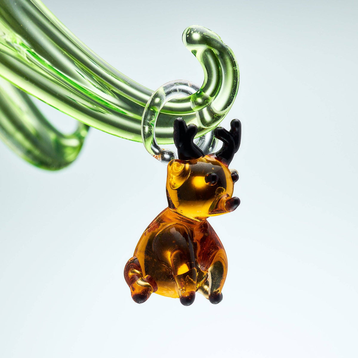Glass reindeer ornament with green glass pipes on a light gray background