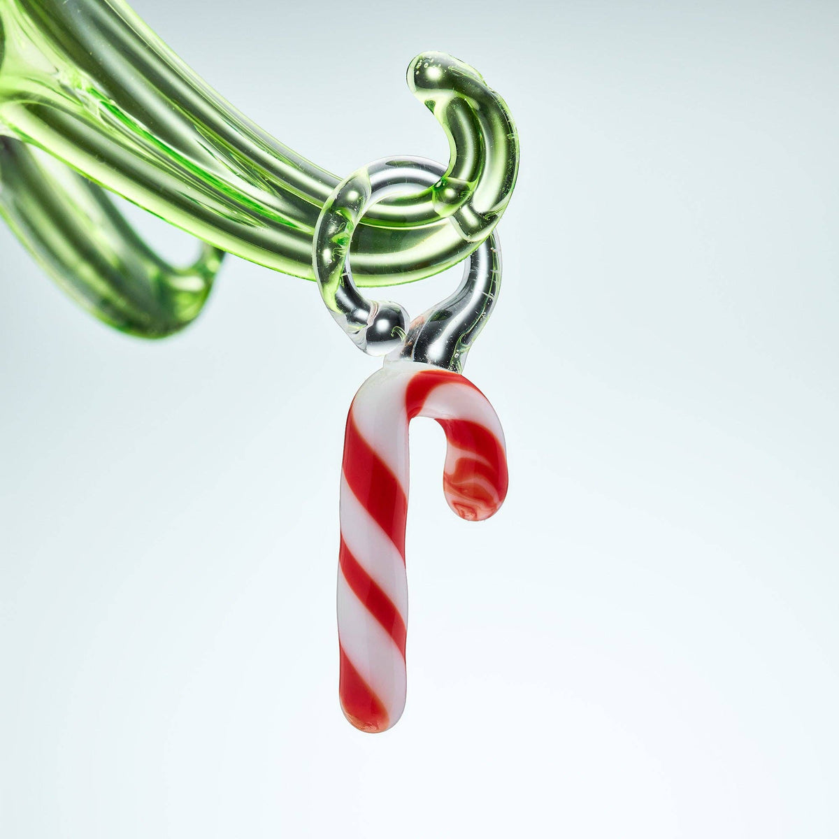 Glass pipe with a candy cane charm on a light gray background
