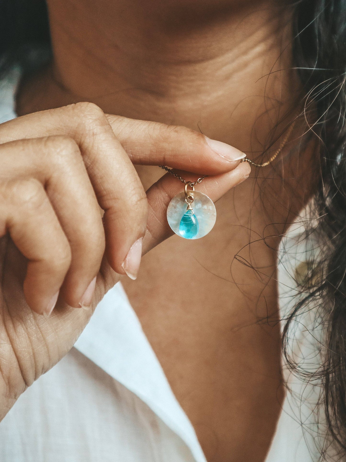 Close-up of a hand holding a necklace with a blue pendant.