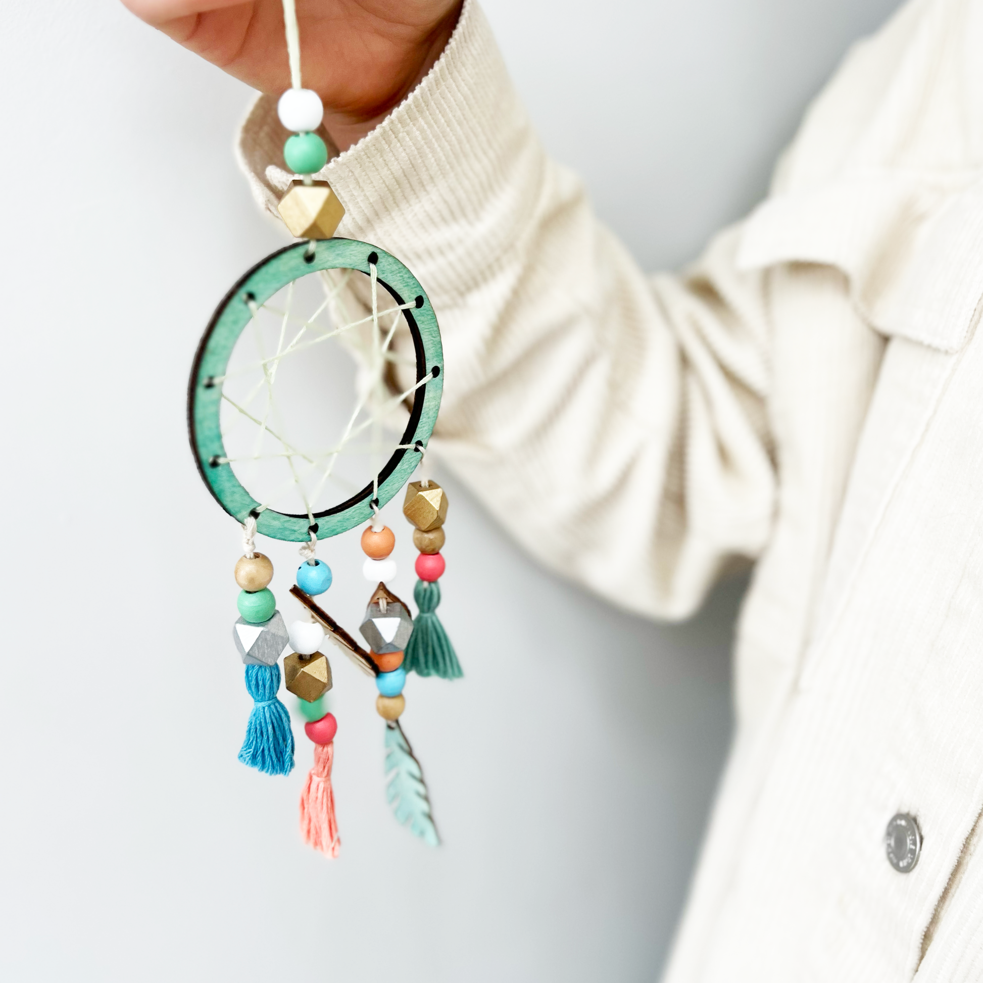 Colorful dreamcatcher held by a person wearing a beige sweater.