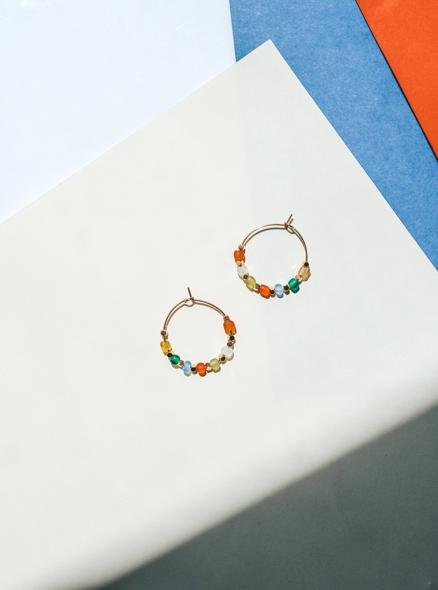 Colorful beaded hoop earrings on a white surface with a colorful background
