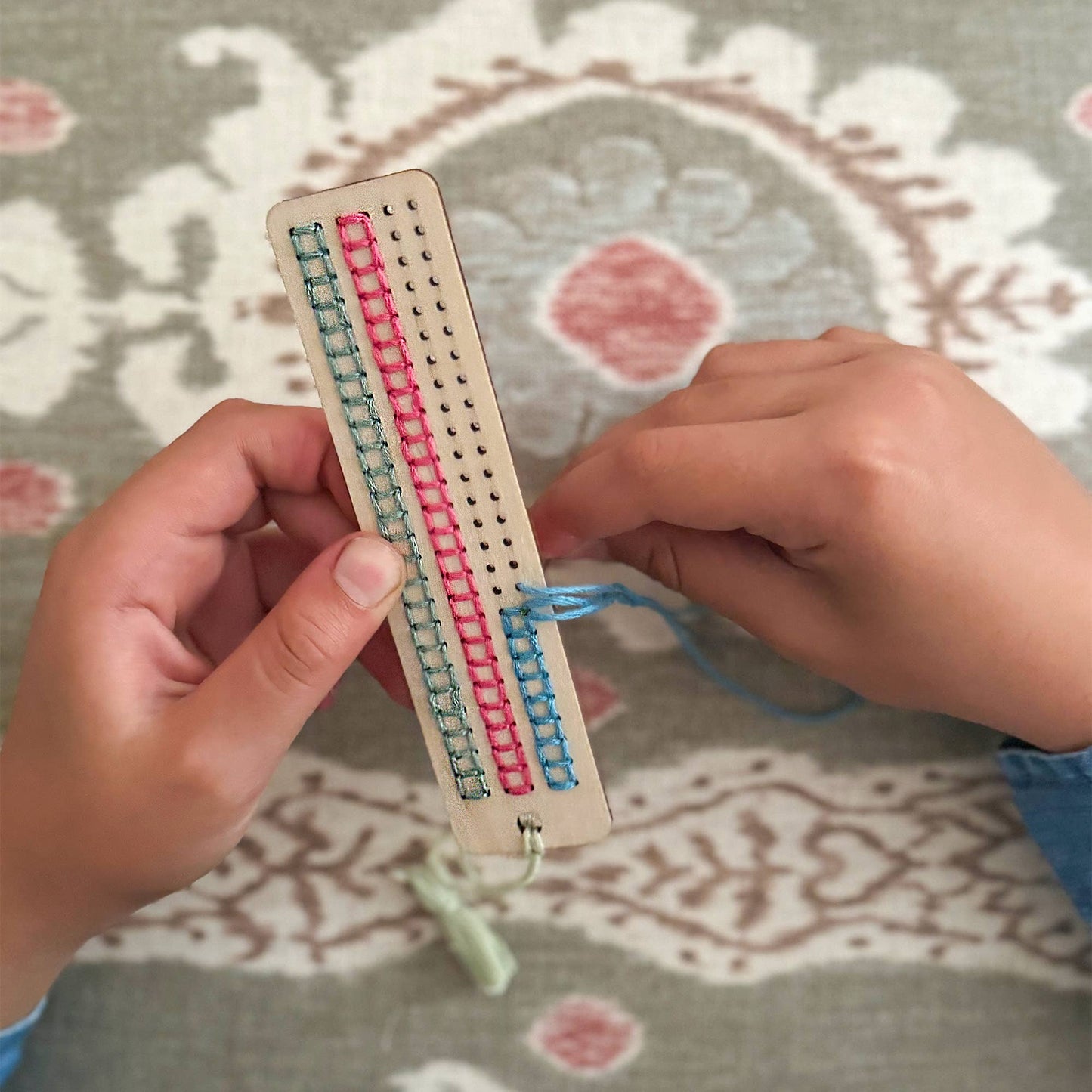 Hands working with a small loom on a patterned fabric background