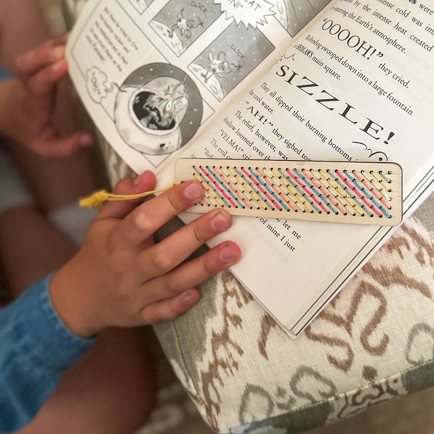 Person holding a colorful bookmark over a book with text and illustrations.