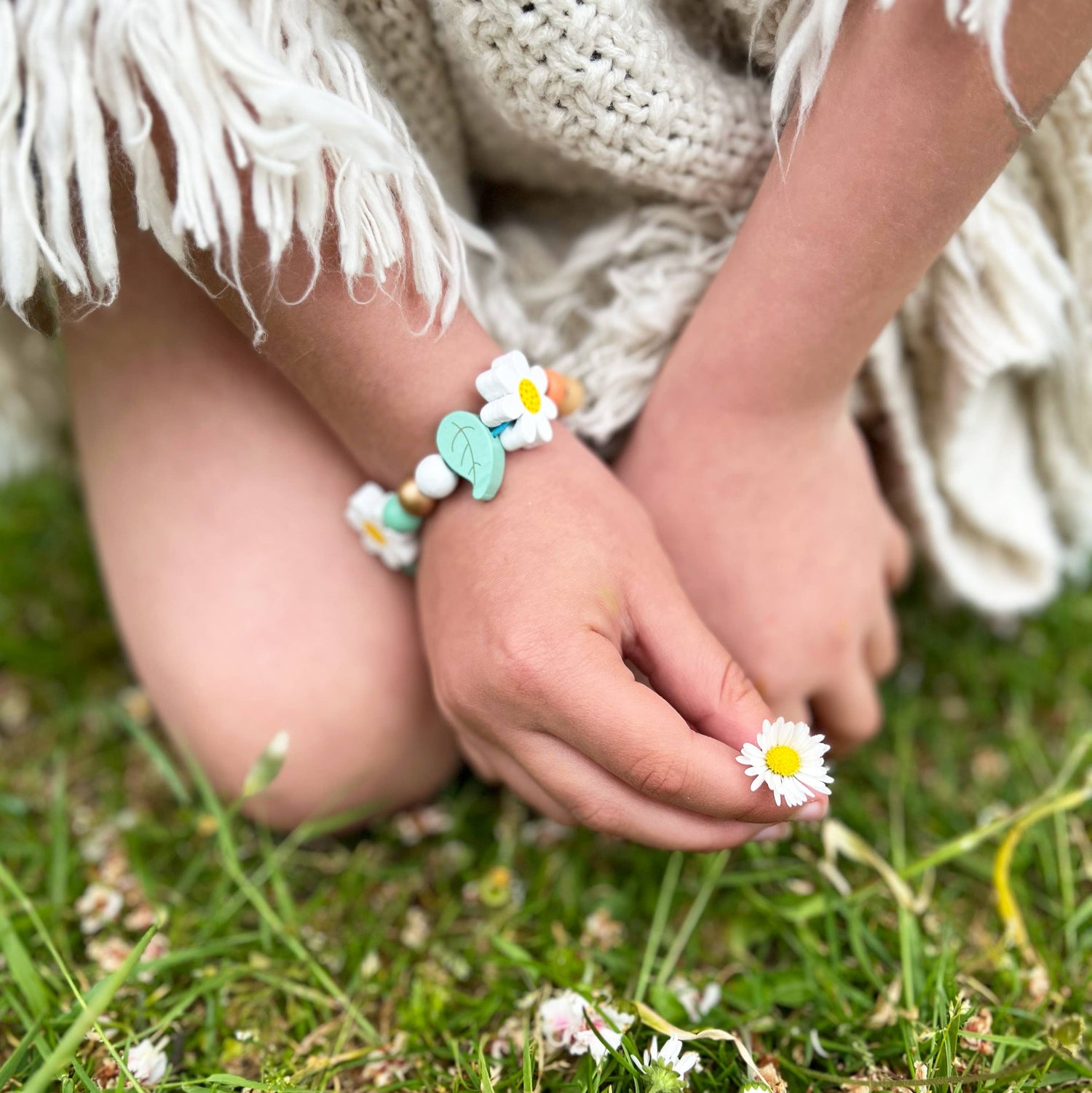 Child's hands wearing a bracelet with flowers on a grassy background