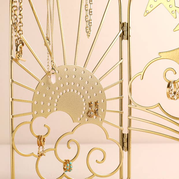 Gold jewelry organizer with necklaces, earrings, and rings on a beige background