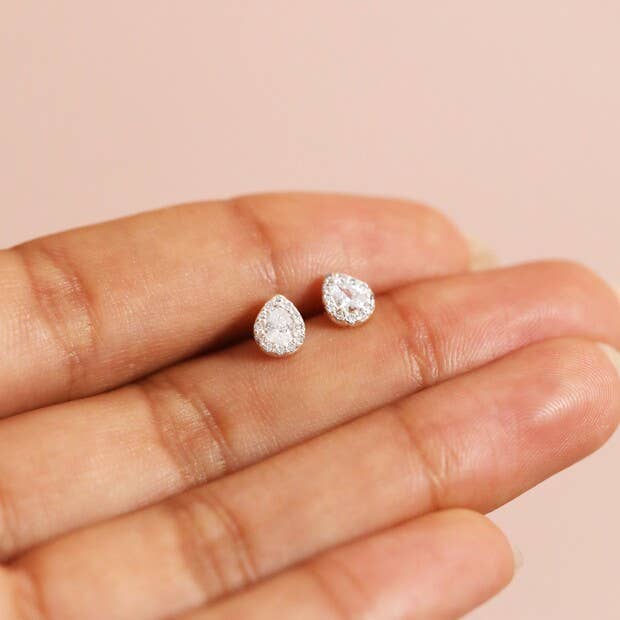 Pear-shaped diamond earrings held between fingers against a pink background