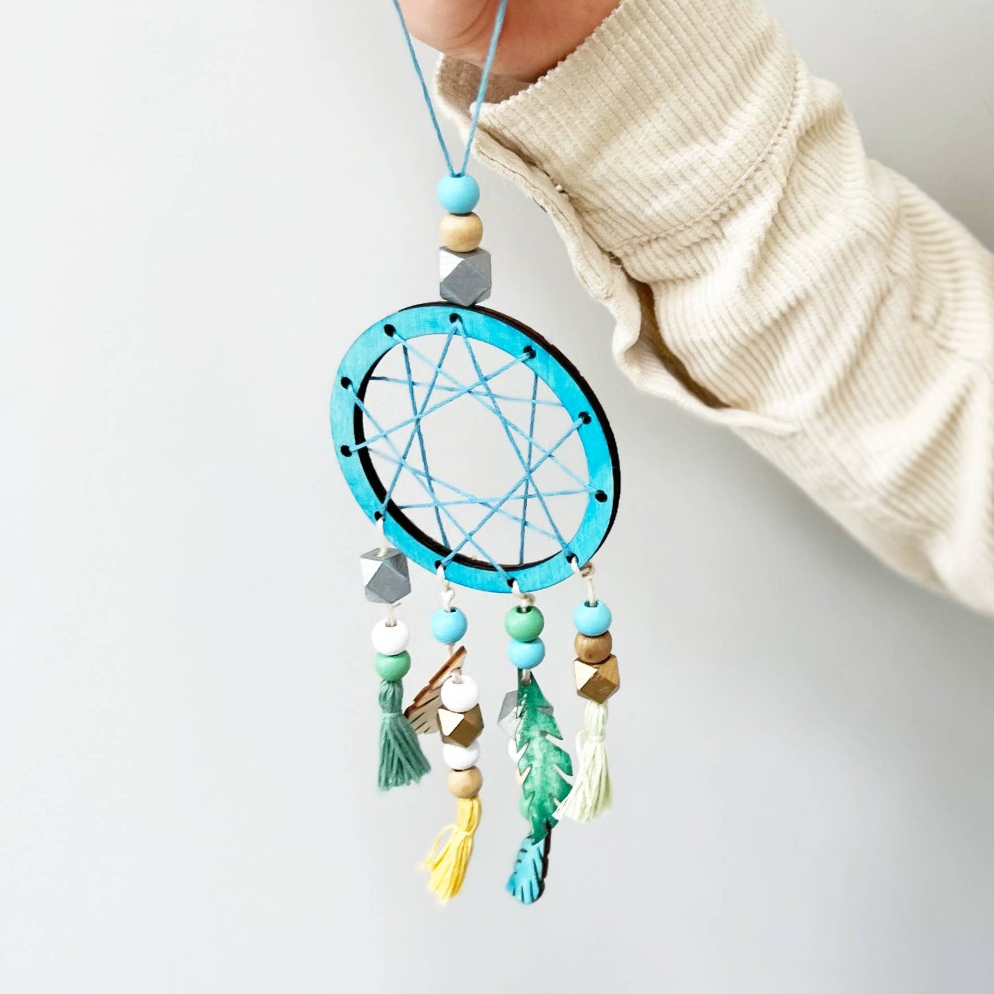 Hand holding a colorful dreamcatcher against a light background