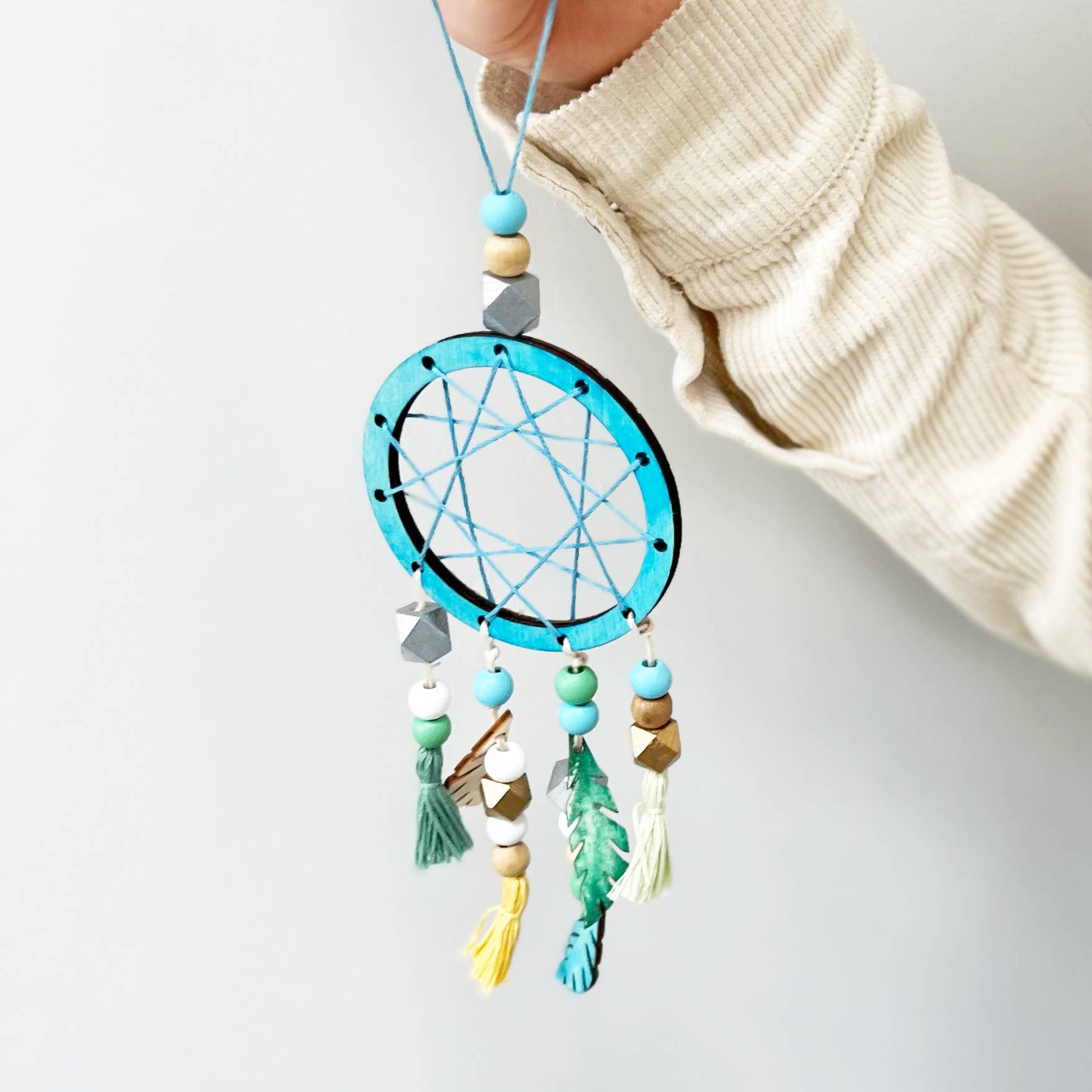 Hand holding a colorful dreamcatcher against a light background