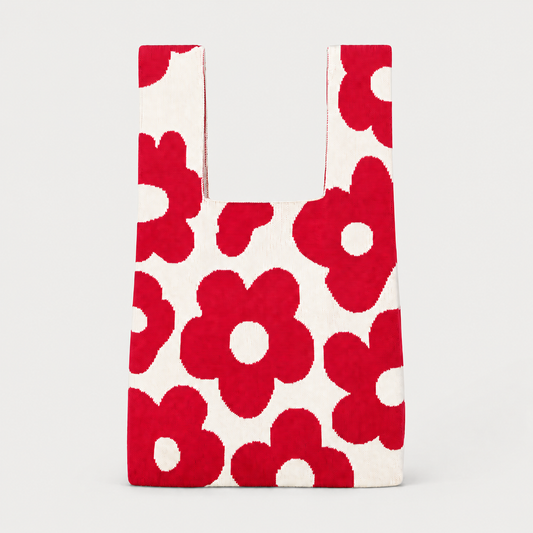 A reusable tote bag with a bold red poppy flower pattern on a white background, shown against a light gray studio backdrop.
