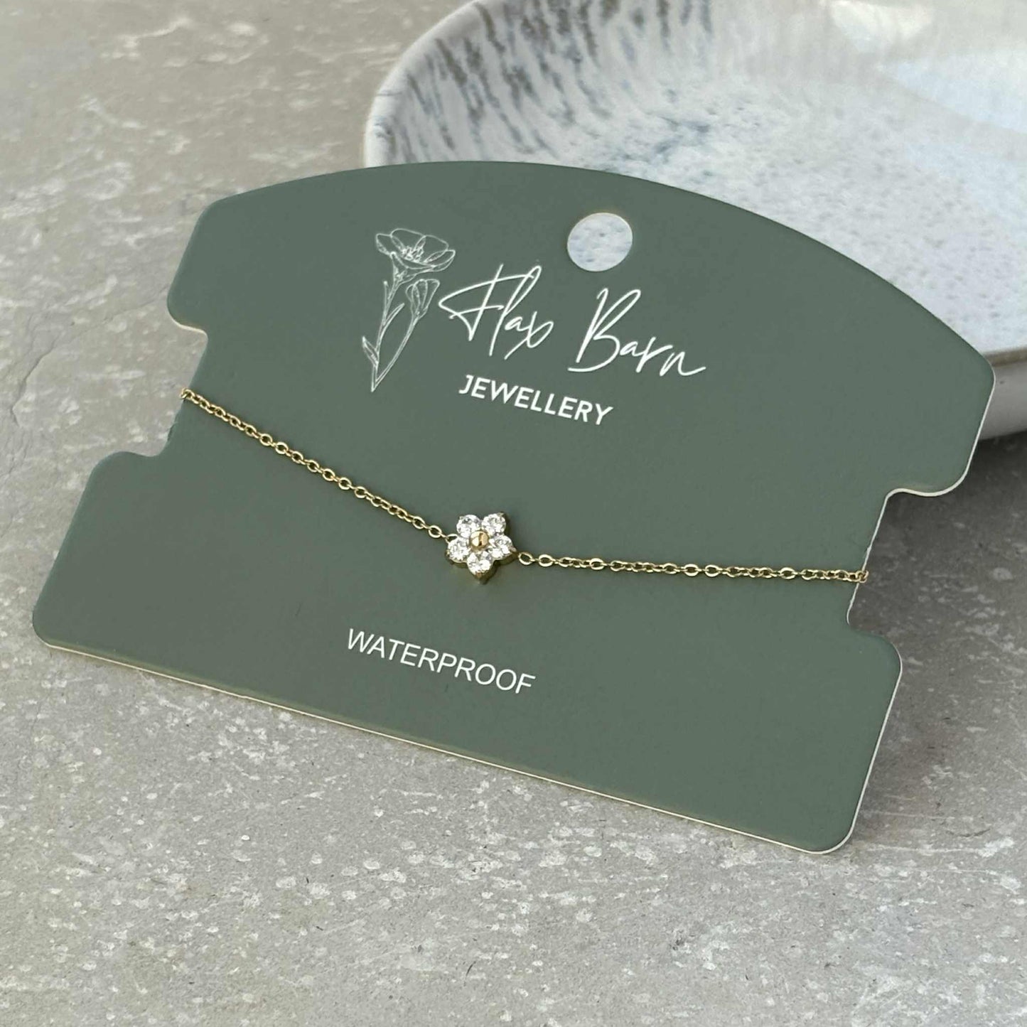 Gold bracelet with a flower charm on a 'Hay Barn Jewellery' card.