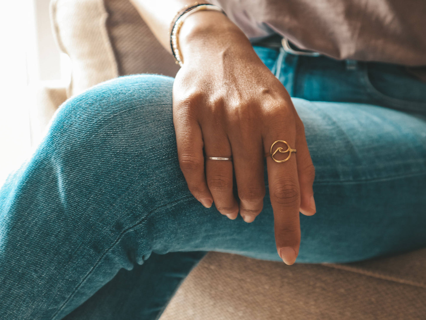 Person wearing teal jeans with a gold ring on a blurred background