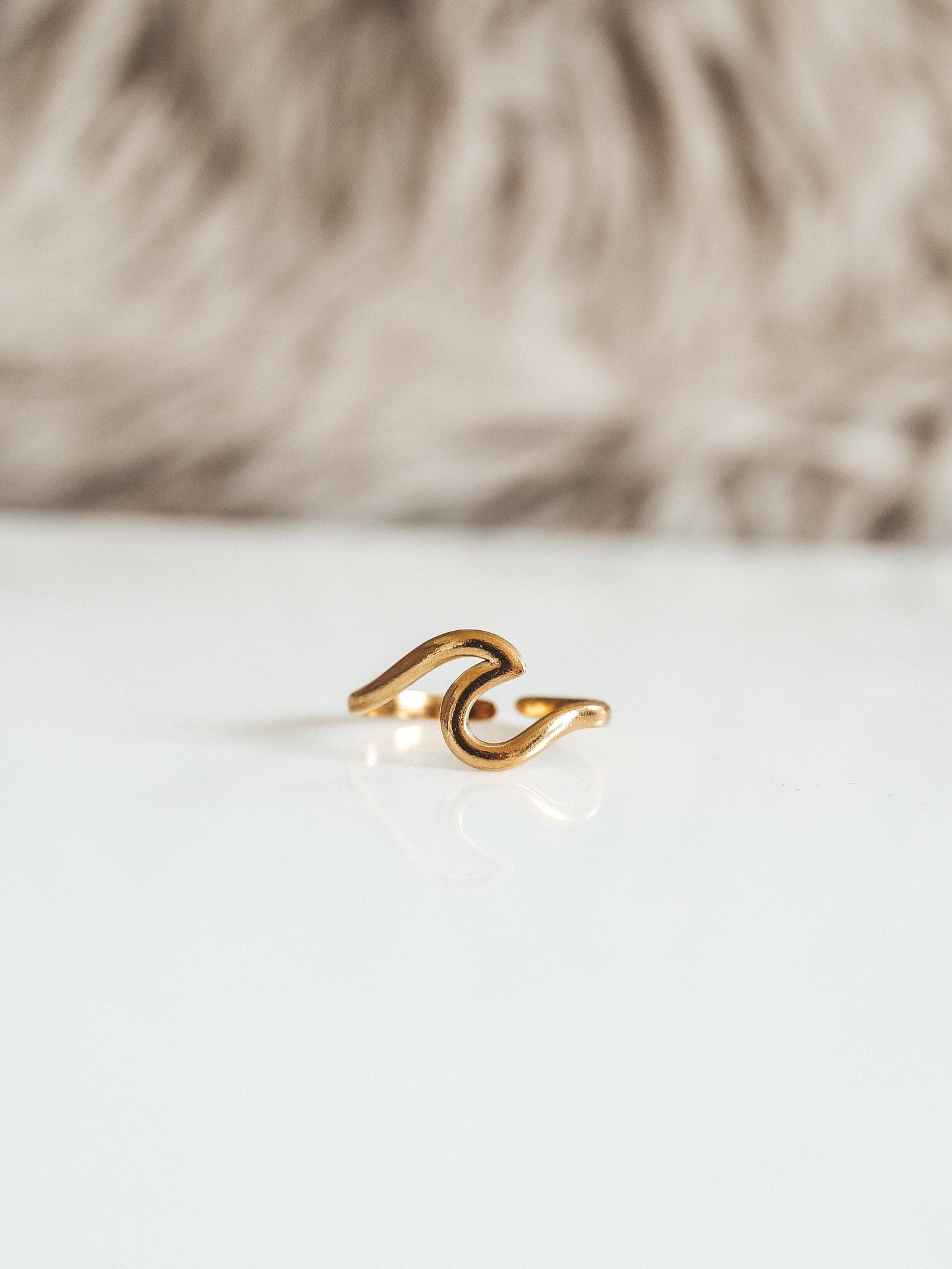 Gold ring with a wave design on a white surface with a blurred background