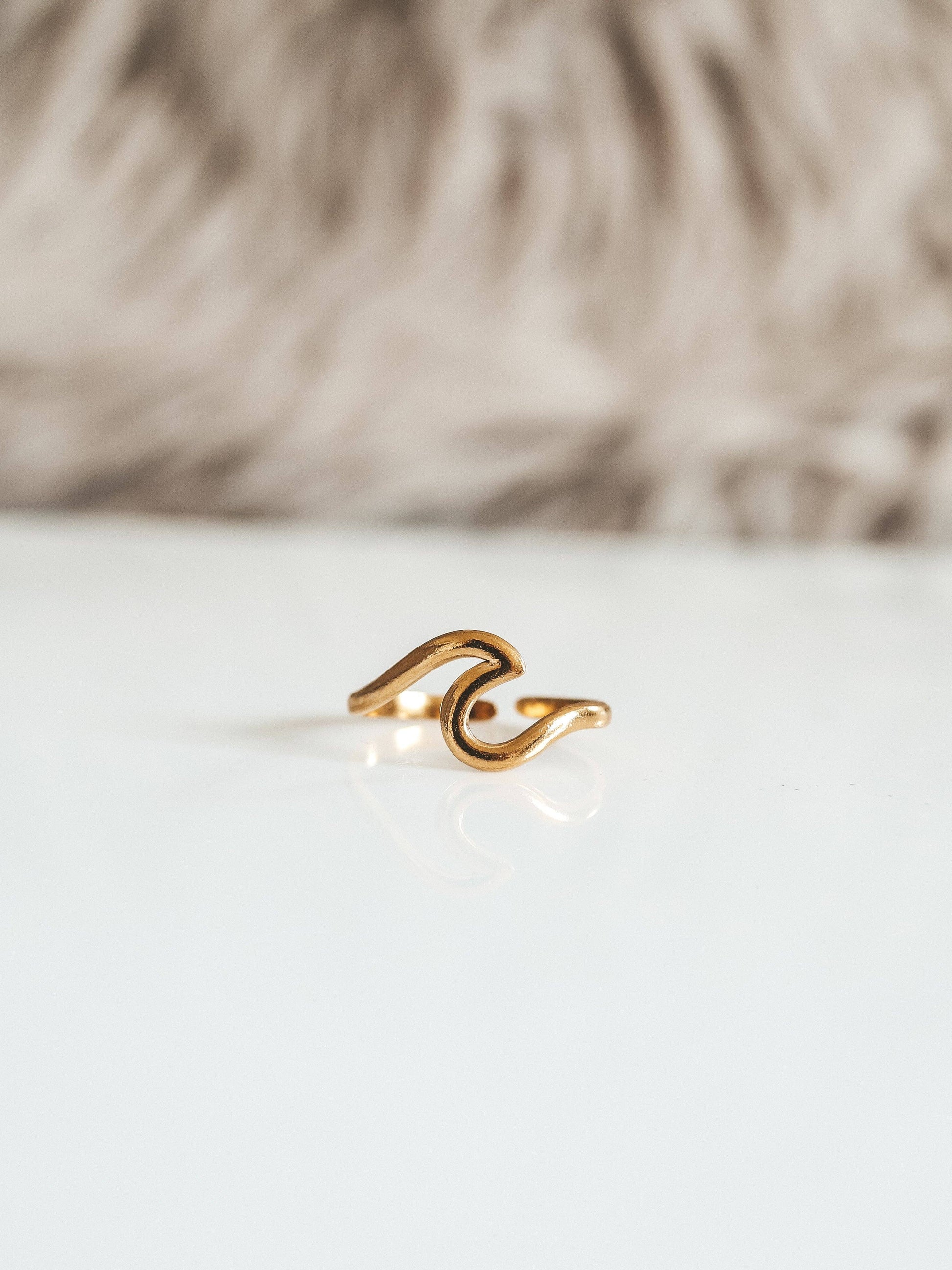 Gold ring with a wave design on a white surface with a blurred background