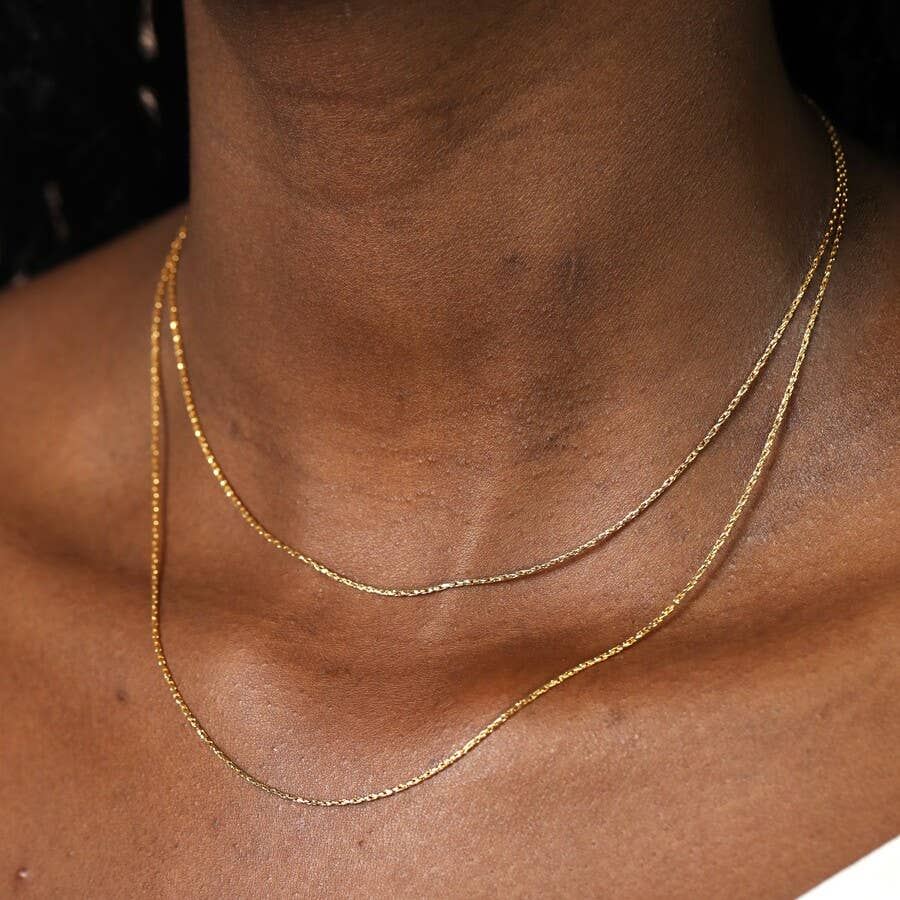 Gold double snake necklace on a person's neck with a dark background