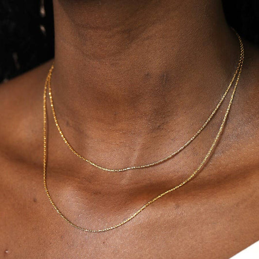 Gold double snake necklace on a person's neck with a dark background