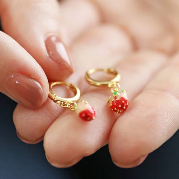 Gold rings with strawberry decorations held in a hand against a blurred background