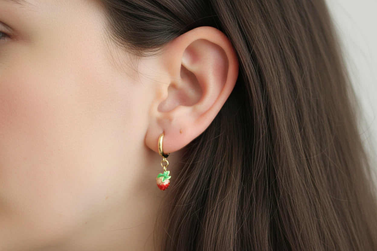 Close-up of an ear wearing a gold hoop earring with a strawberry charm.