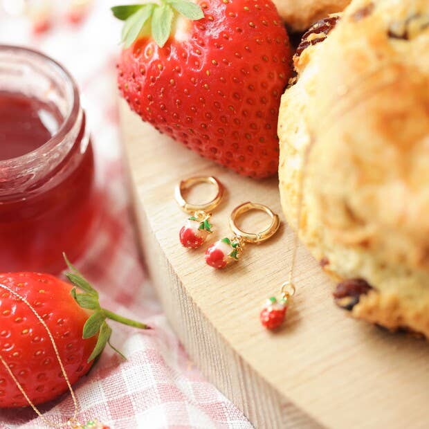 Strawberry-themed earrings on a wooden board with strawberries and scones.