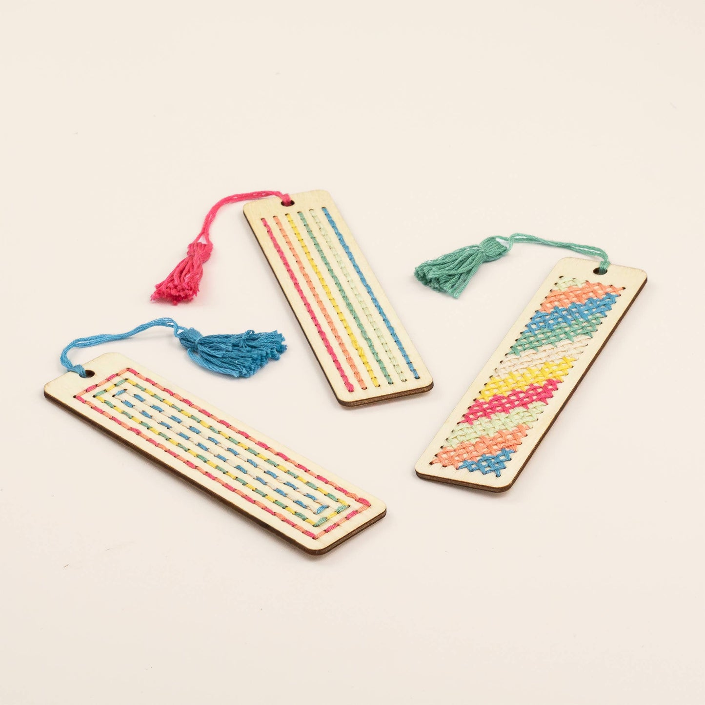Three wooden bookmarks with colorful thread patterns on a light beige background