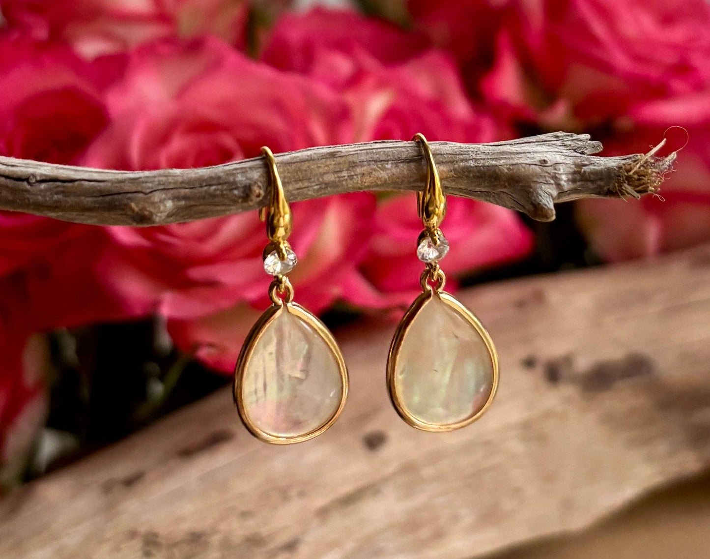 Gold teardrop earrings with clear stones on a branch with pink flowers in the background
