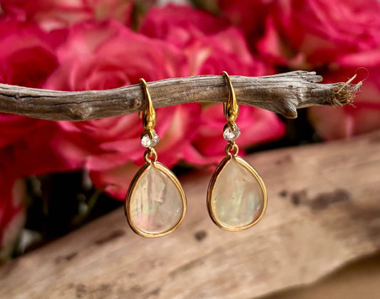 Gold teardrop earrings with clear stones on a branch with pink flowers in the background