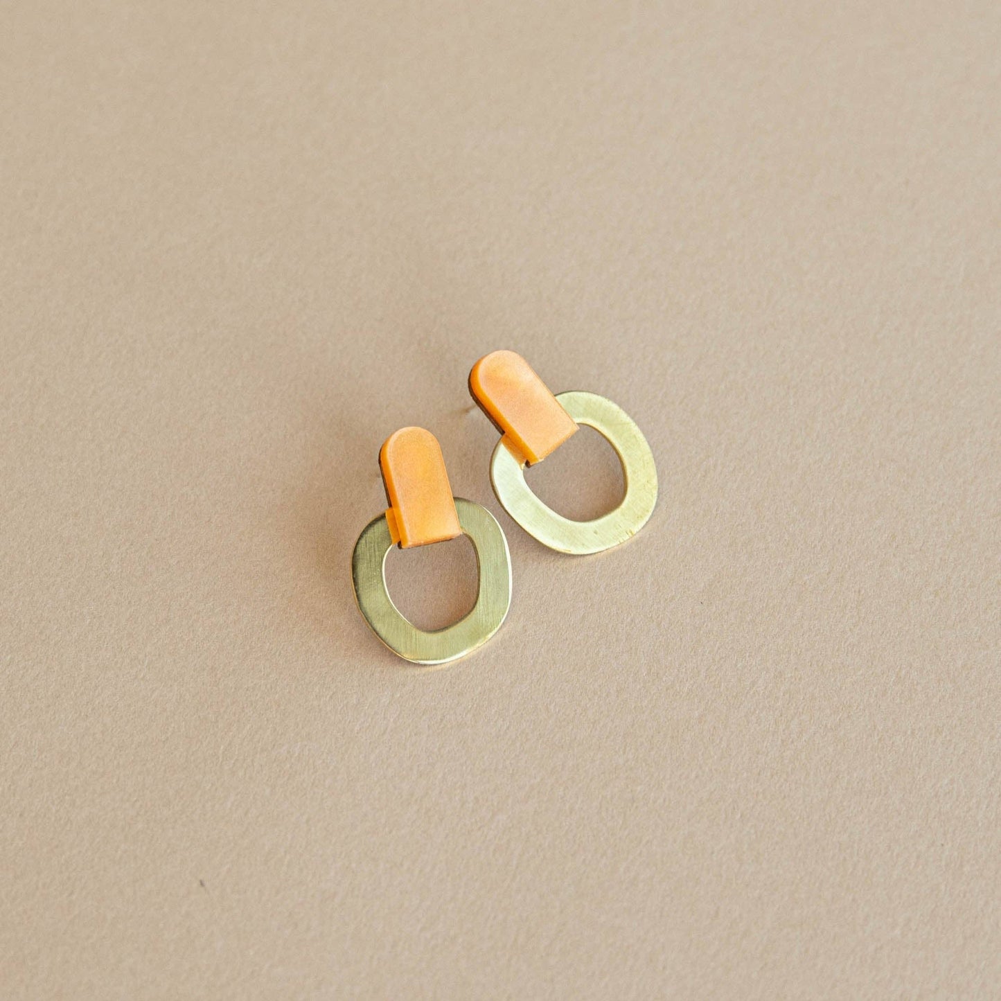 Orange brass stud earrings handmade in the UK from FSC wood, recycled brass and acrylic with nickel-free posts on light beige background.