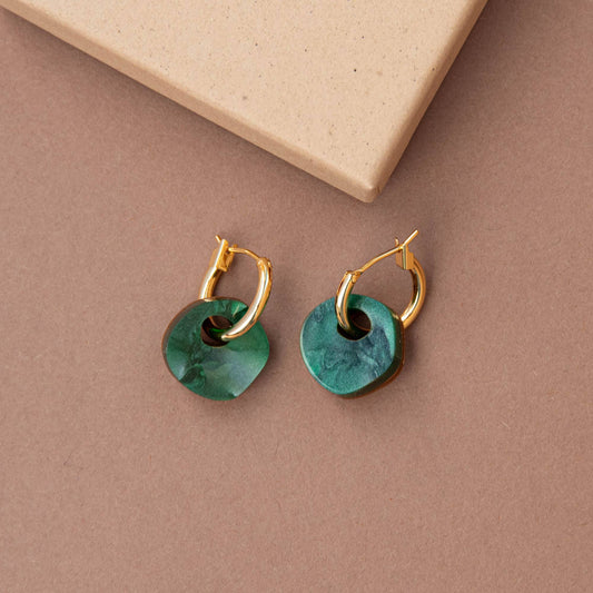 Gold earrings with green circular stones on a beige background