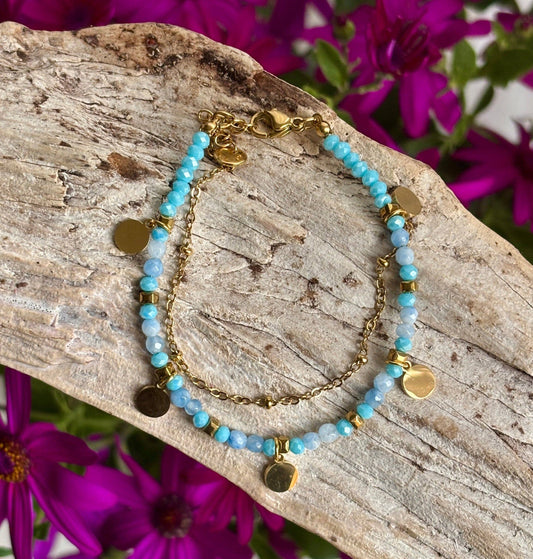 Turquoise beaded bracelet with gold accents on a wooden surface with purple flowers in the background